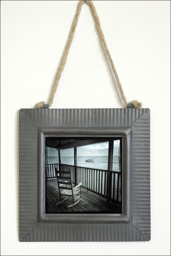 fine art print on metal with tin frame of a wooden rocking chair on porch watching shrimp boat on the ocean at sea, moody nostalgic